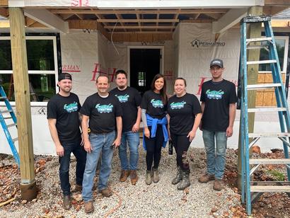 Group of six people in matching shirts standing in front of a house under construction.