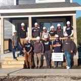 A group of people in hard hats pose in front of a partially built house with a "Thank you Groundworks" sign.
