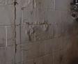 A damp, cracked basement wall with a pipe fixture and visible water stains.