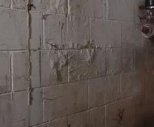 A damp, cracked basement wall with a pipe fixture and visible water stains.