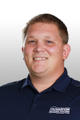 Smiling person wearing a navy blue polo shirt with a logo, against a white background.