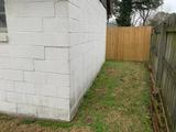 Side of a white building, wooden fence on the right, grass and trees in the background.