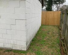 Side of a white building, wooden fence on the right, grass and trees in the background.