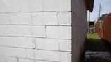 A white cinder block wall forming a building's corner, with grass and a wooden fence in the background.