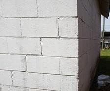 A white cinder block wall forming a building's corner, with grass and a wooden fence in the background.