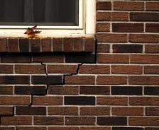 A crack runs through a brick wall beneath a window with a few fallen leaves on the windowsill.