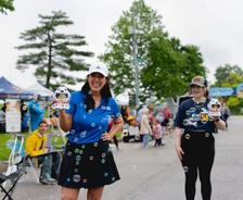Two women smiling outdoors, holding bubble-blowing toys, surrounded by bubbles and people at an event.