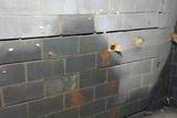 Cracked concrete block wall with visible damage and water stains in an unfinished basement.