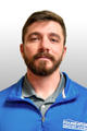 Man with short brown hair and beard wearing a blue jacket and gray shirt, posing against a light background.