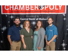 Four smiling people stand in front of a "Chamberopoly" event banner at the Moberly Chamber of Commerce banquet.