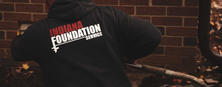 Person in Indiana Foundation Service sweatshirt working with tools near a brick wall.