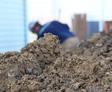 closeup of a pile of dirt with a man grading the soil in the background