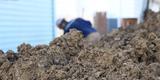 closeup of a pile of dirt with a man grading the soil in the background