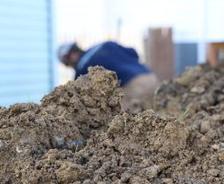 closeup of a pile of dirt with a man grading the soil in the background