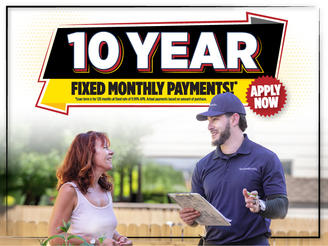 A smiling man with a clipboard talks to a woman under a sign reading "10 Year Fixed Monthly Payments! Apply Now.