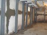 Basement with reinforced concrete walls, steel beams for support, ductwork on ceiling, and a small window.
