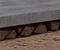Close-up of concrete slab supported by angled brown rocks, atop a textured brown surface, highlighting the interplay with foundation soils.