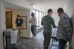 Four people casually talking and interacting in a hallway near a table with snacks and drinks.