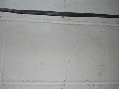 Cracked white brick wall with a black cable running along the top.