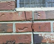 A brick wall with a noticeable vertical crack below a screened window may indicate underlying foundation problems.