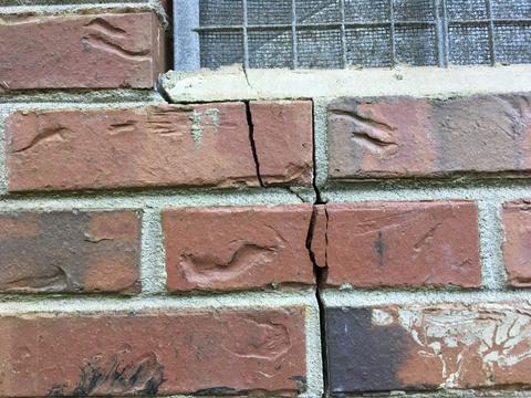 A brick wall with a noticeable vertical crack below a screened window may indicate underlying foundation problems.