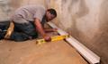 Person using a level tool to install a baseboard on a concrete floor near a wall.