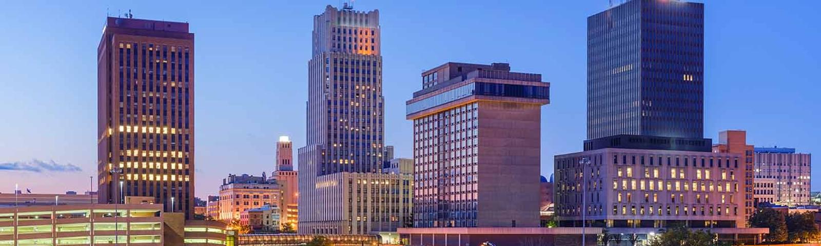 City skyline at dusk with tall buildings and a clear blue sky.