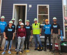 A group of volunteers in hard hats stand in front of a newly built house.