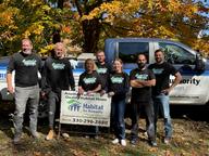 A group of people in matching shirts posing outdoors in front of a truck and a Habitat for Humanity sign.