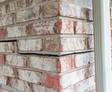 Close-up of cracked brick wall with misaligned bricks next to a vertical white gutter.