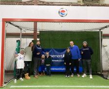 A group of people, including children, standing and posing inside an indoor soccer goal.